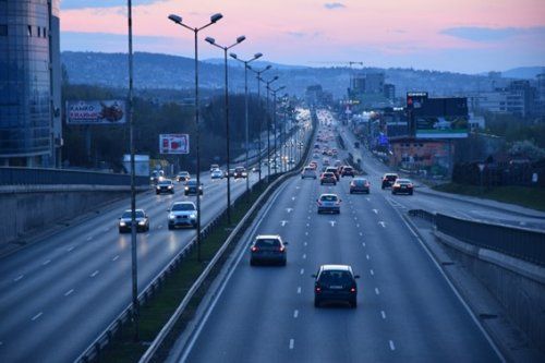 Imagen de una carretera con tres carriles y coches circulando por ella por una ciudad Imagen de una carretera con tres carriles y coches circulando por ella por una ciudad